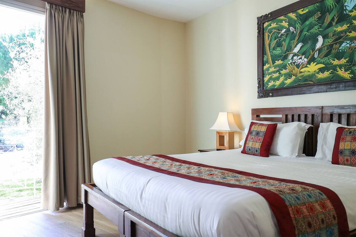 Habitación de hotel con una cama grande, un cuadro de una escena selvática y vistas al exterior con vegetación.
