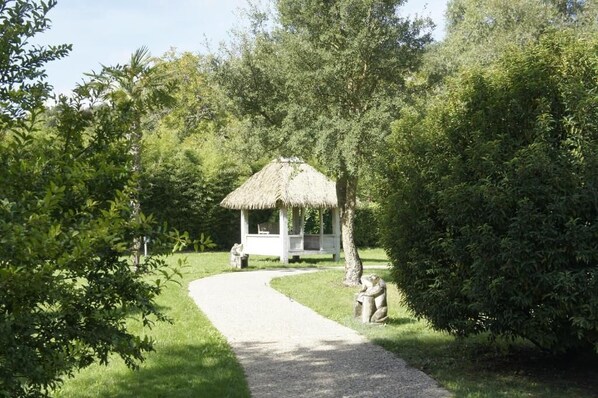 Ein Pavillon mit Strohdach in einem üppigen Garten, verbunden durch einen Kiesweg.