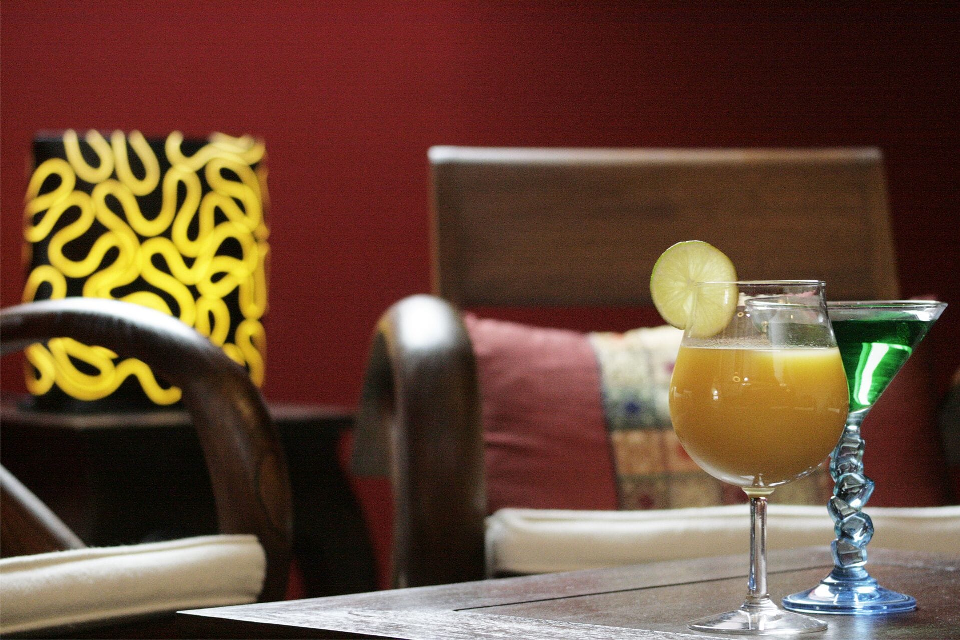 Une table avec deux verres contenant des boissons, dont l’un est décoré d’une tranche de citron vert, et une chaise avec un coussin à motifs.