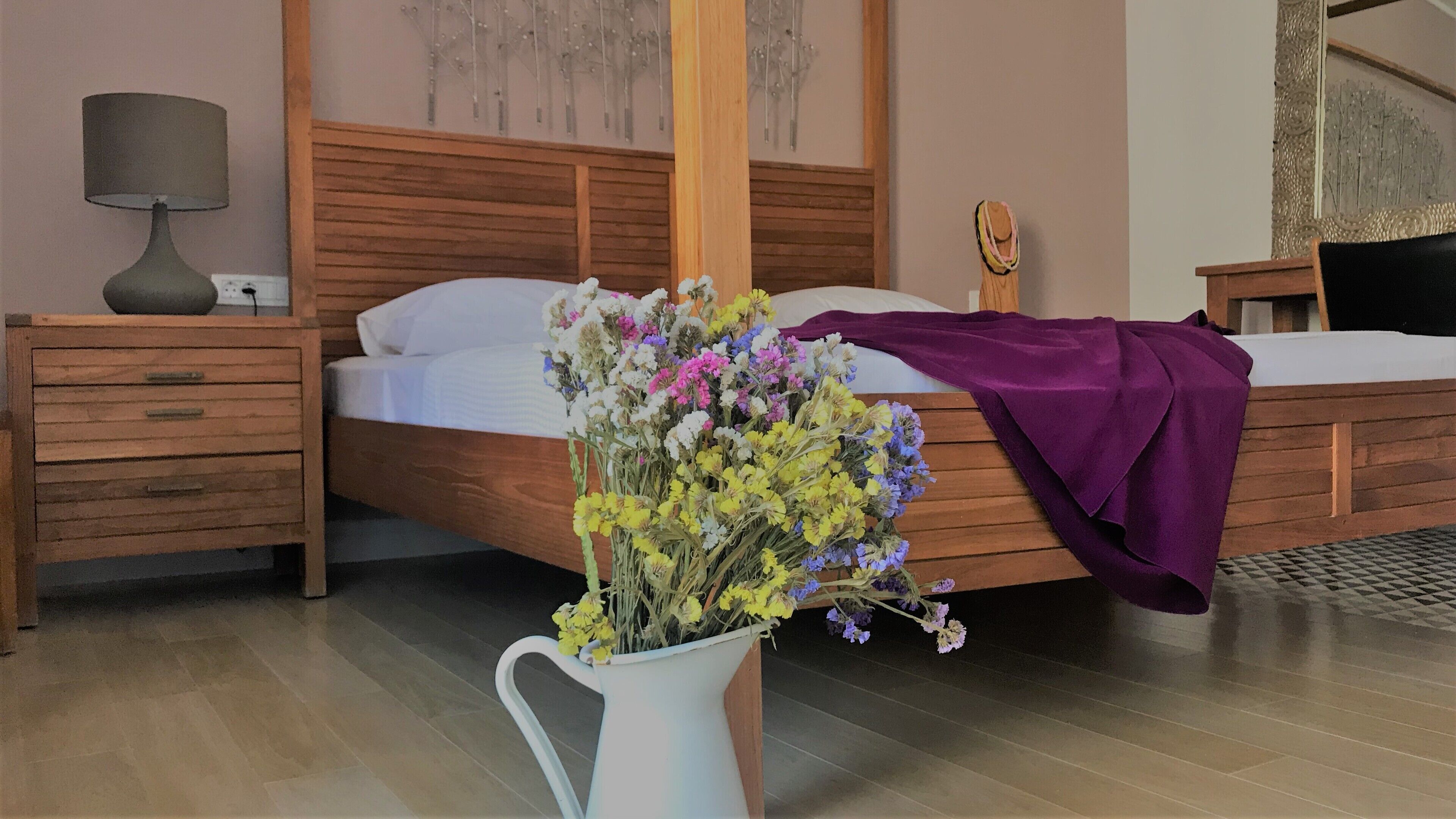 A bedroom with a wooden bed, a nightstand with a lamp, and a vase of flowers.