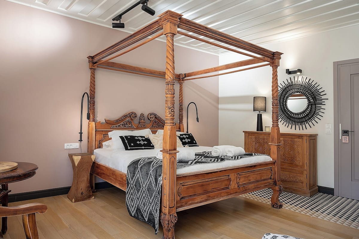 A four-poster bed with a wooden finish, a bedside table, a mirror, and a cabinet.