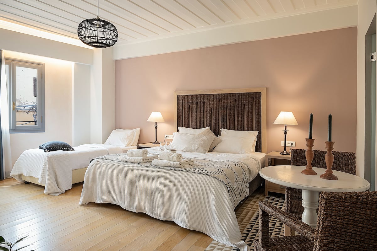A hotel room with two beds, a round table, wicker chairs, and a large window.