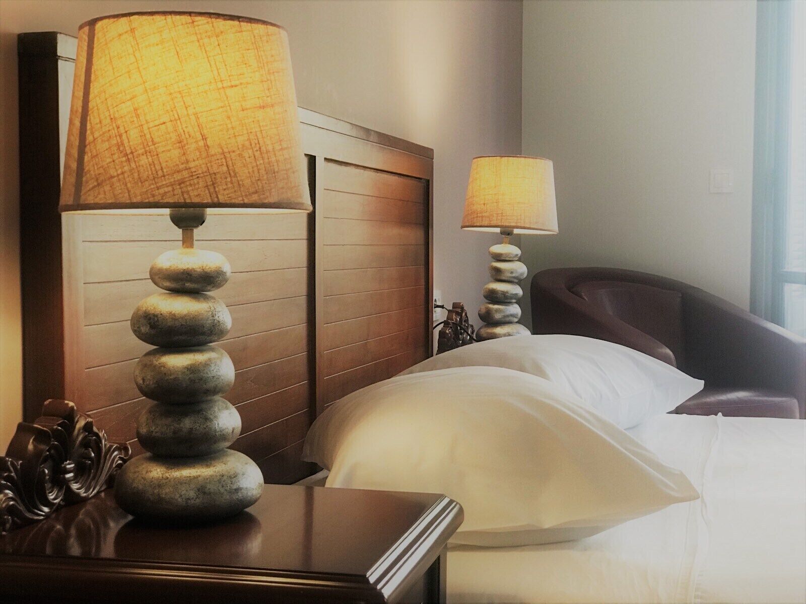 Une chambre d’hôtel avec une tête de lit en bois, un lit recouvert de draps blancs et deux lampes de chevet dotées d’abat-jour texturés.