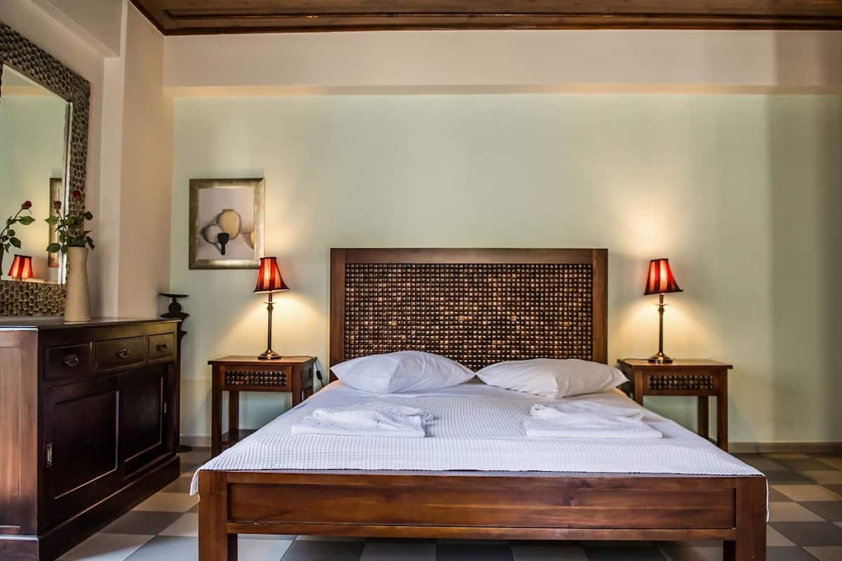 A neatly made bed with white linens, two bedside lamps, a wooden headboard, a dresser, and a framed picture on the wall.
