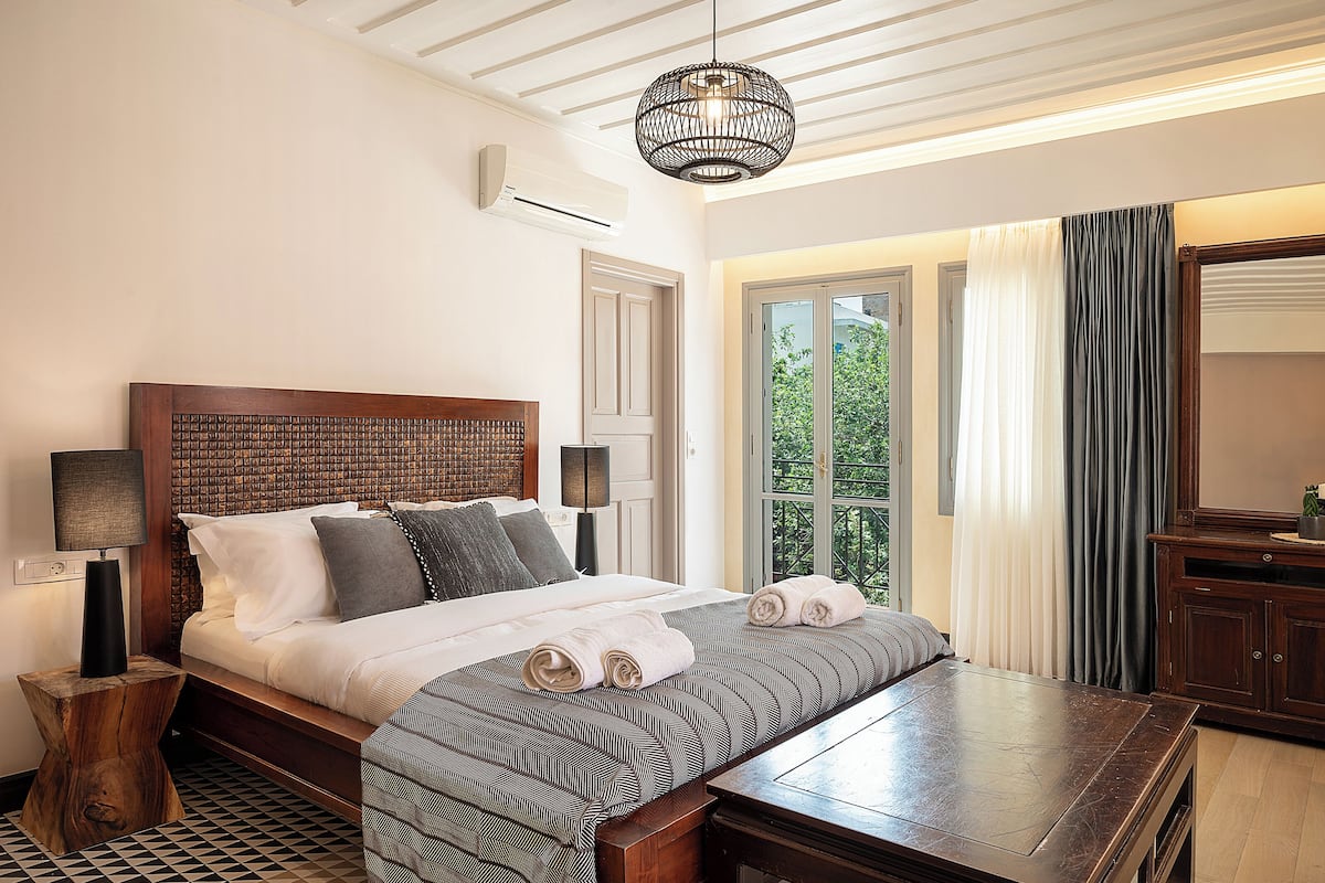 A neatly made bed with a patterned bedspread, a bedside table, and a hanging light fixture.