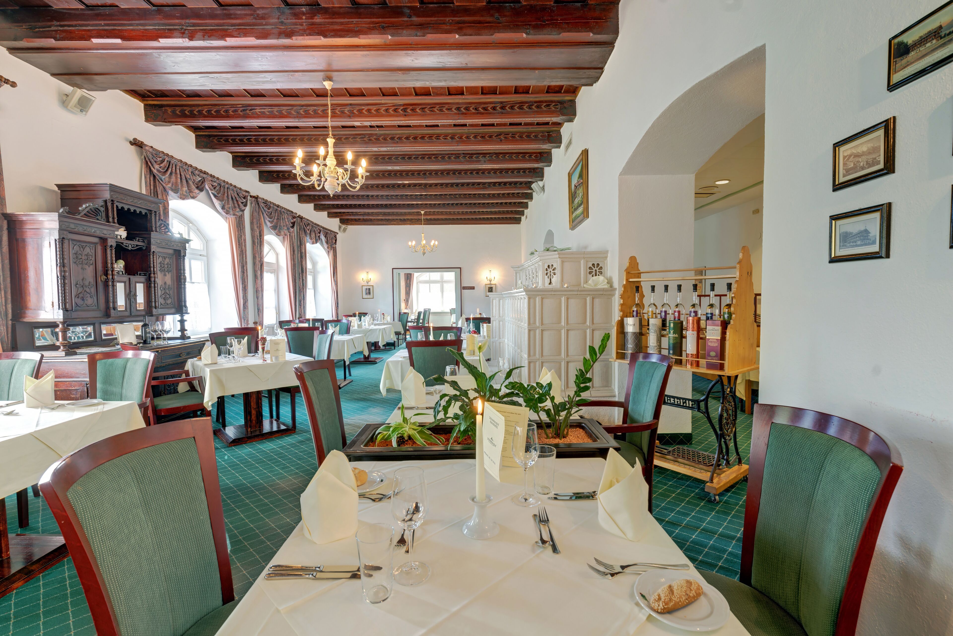 A restaurant with wooden beams, green chairs, white tables, and a chandelier.