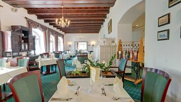 A restaurant with wooden beams, green chairs, white tables, and a chandelier.