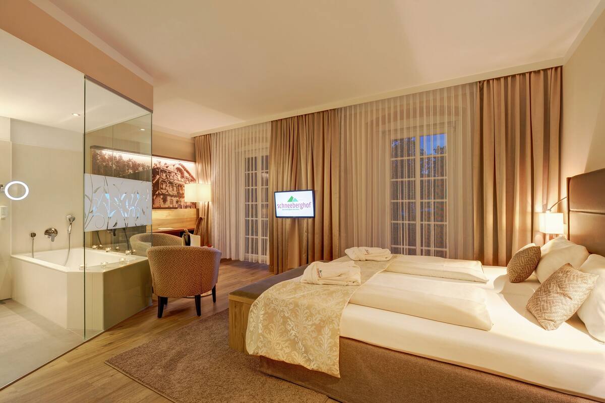 Habitación de hotel con una cama grande, un área de descanso con una silla, una bañera y una pantalla de televisión.