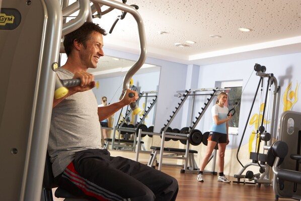 Un gimnasio con equipo de ejercicio, espejos y suelo de madera.