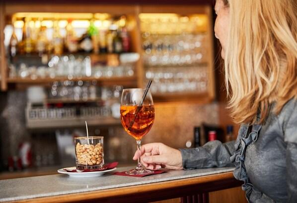A bar setting with a person holding a glass of amber-colored drink.