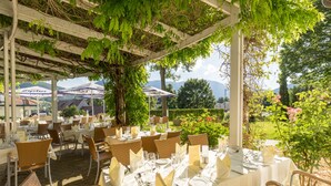 An outdoor dining area with tables set for a meal, surrounded by greenery and a view of mountains. - Schneeberghof (Puchberg Am Schneeberg)