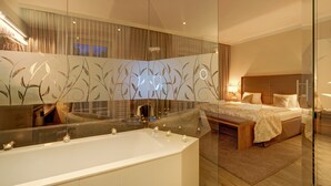 A modern bedroom with a large bed, a glass-enclosed bathtub, and a large mirror reflecting the room. - Schneeberghof (Puchberg Am Schneeberg)