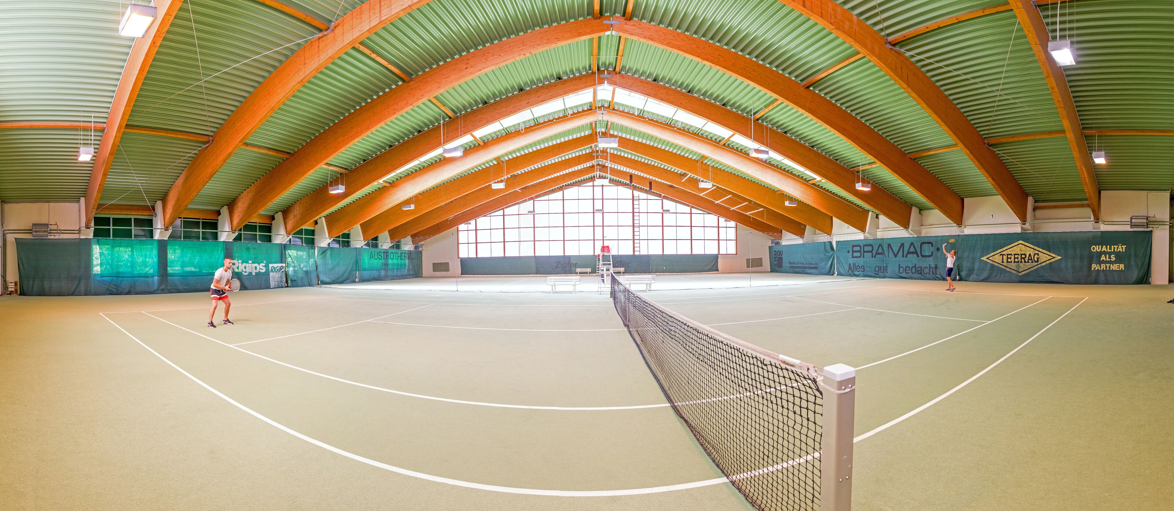 Ein Hallen-Tennisplatz mit hoher Decke und Holzbalken.