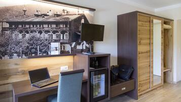 A compact hotel room with a wooden desk, a laptop, a chair, a television, and a wardrobe with a mirror.