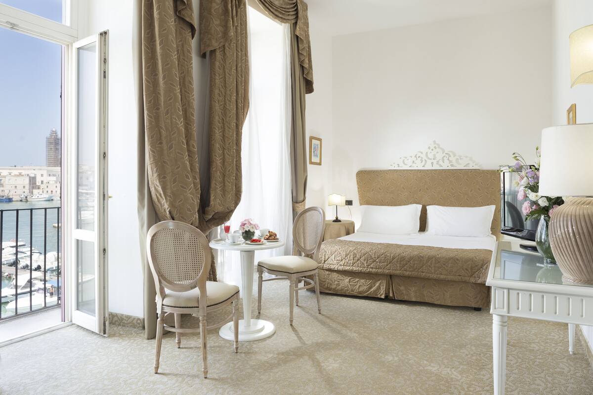 A hotel room with a bed, a table with chairs, a window with curtains, and a view of the city.