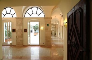 A spacious lobby with arched windows, a central door, and a chandelier. - Hotel San Paolo al Convento (Trani)