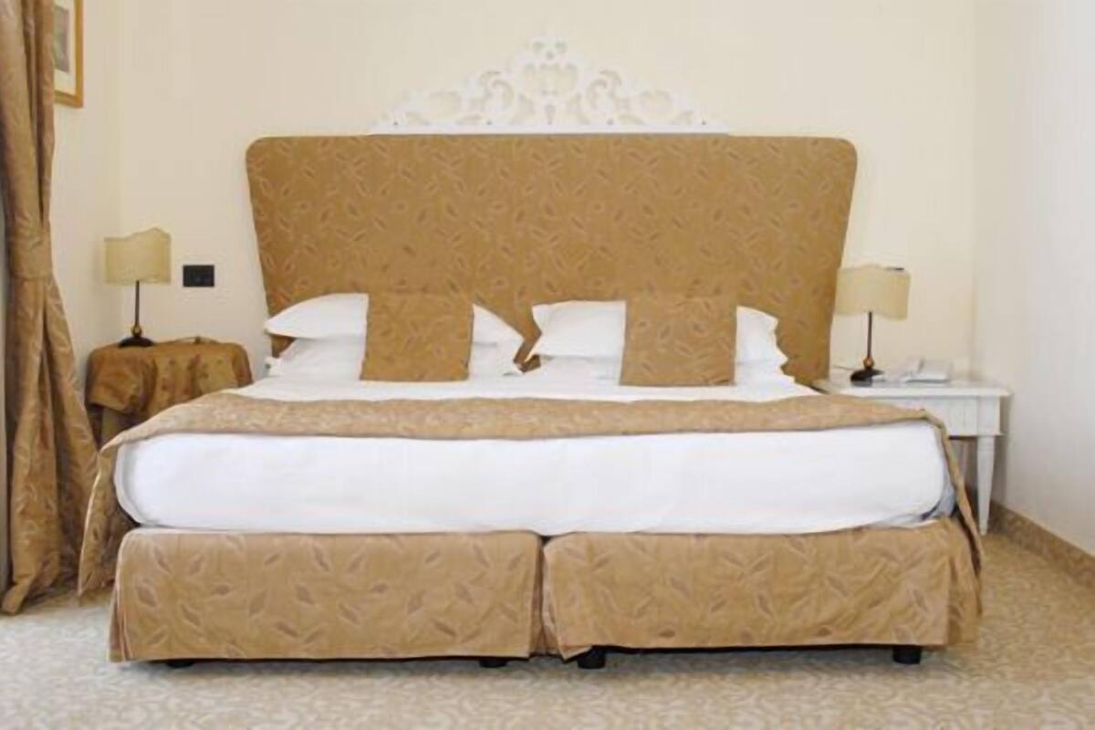 A double bed with a patterned headboard and footboard, two bedside tables with lamps, and a carpeted floor.