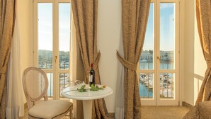 A room with a view of a body of water, a table with a bottle and glasses, a chair, and curtains. - Hotel San Paolo al Convento (Trani)