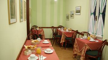 A dining area with multiple tables set for breakfast, featuring bread, pastries, and juice.