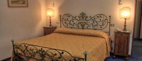 A single bed with a metal frame and ornate headboard, flanked by two bedside tables with lamps.