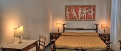 A bedroom with a wooden bed, two bedside tables, a desk, and a chair. There is a painting on the wall and a lamp on each bedside table.