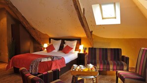 A cozy, rustic bedroom with a large bed, striped armchairs, and a breakfast tray.