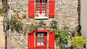 A stone building with red shutters and a small porch.