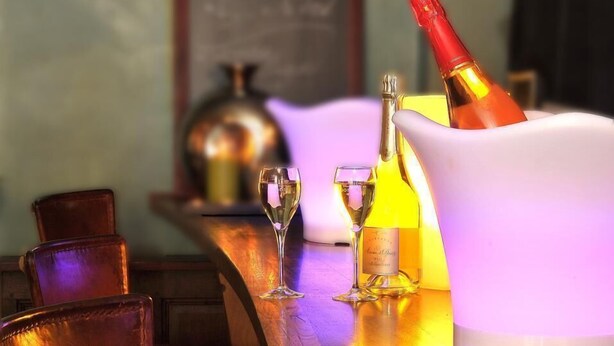 A bar area with a bottle of champagne, glasses, and a chalkboard menu in the background.