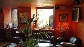 A cozy restaurant interior with leather chairs, a large potted plant, and a window with natural light.