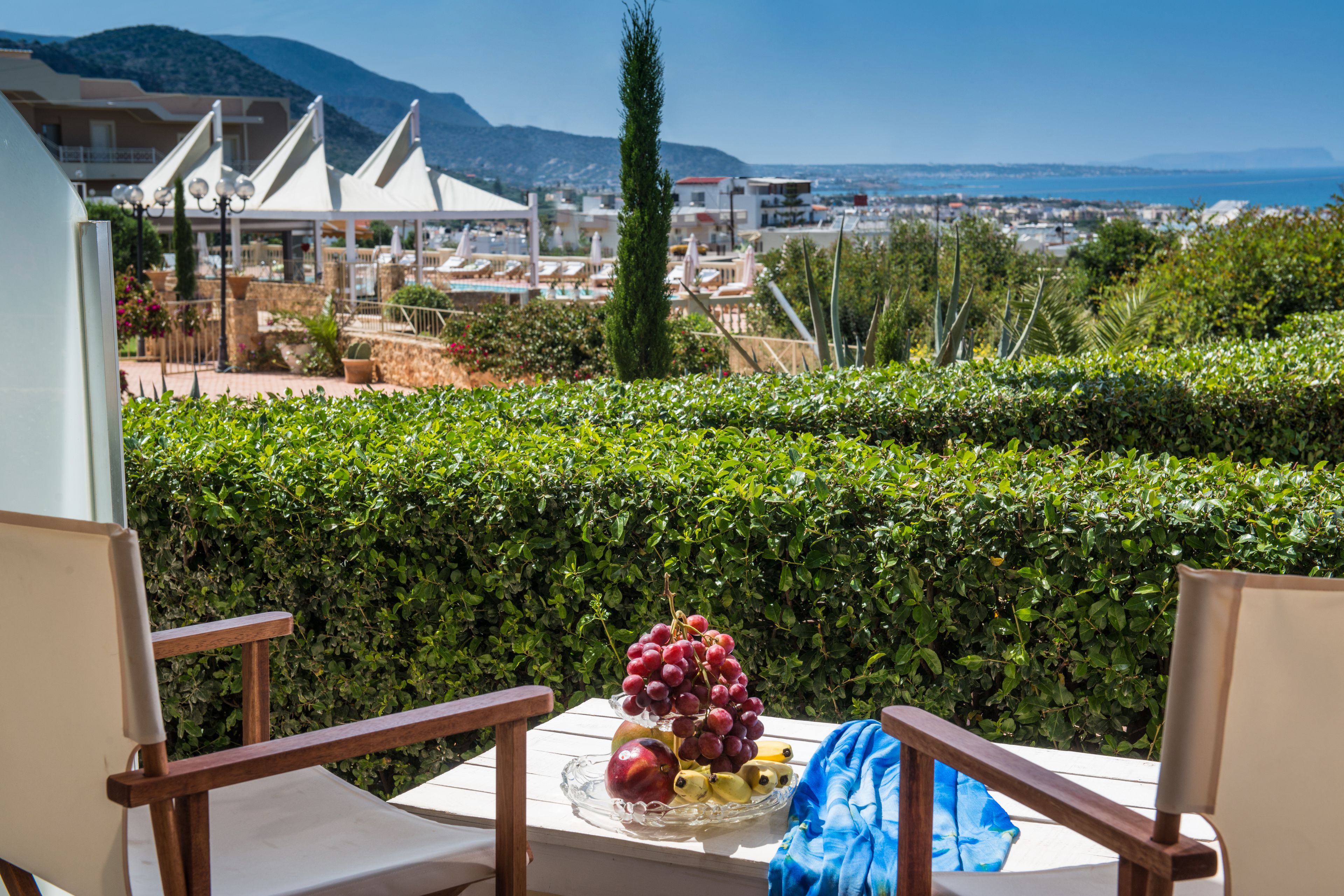 Un balcón con una mesa dispuesta con fruta, con vistas a un pueblo costero con edificios y una montaña al fondo.