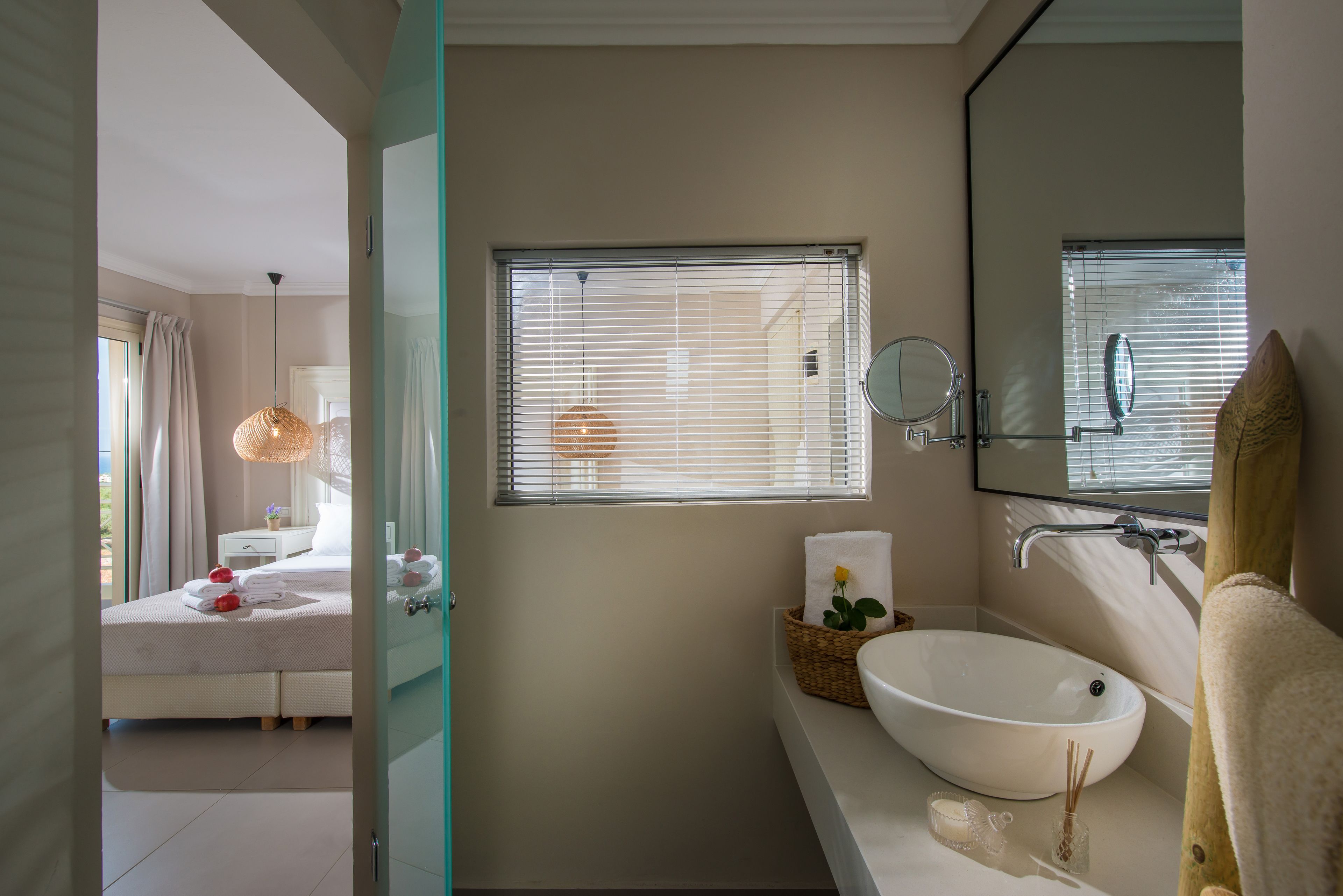 A modern bathroom with a large mirror, a white sink, and a window with blinds.