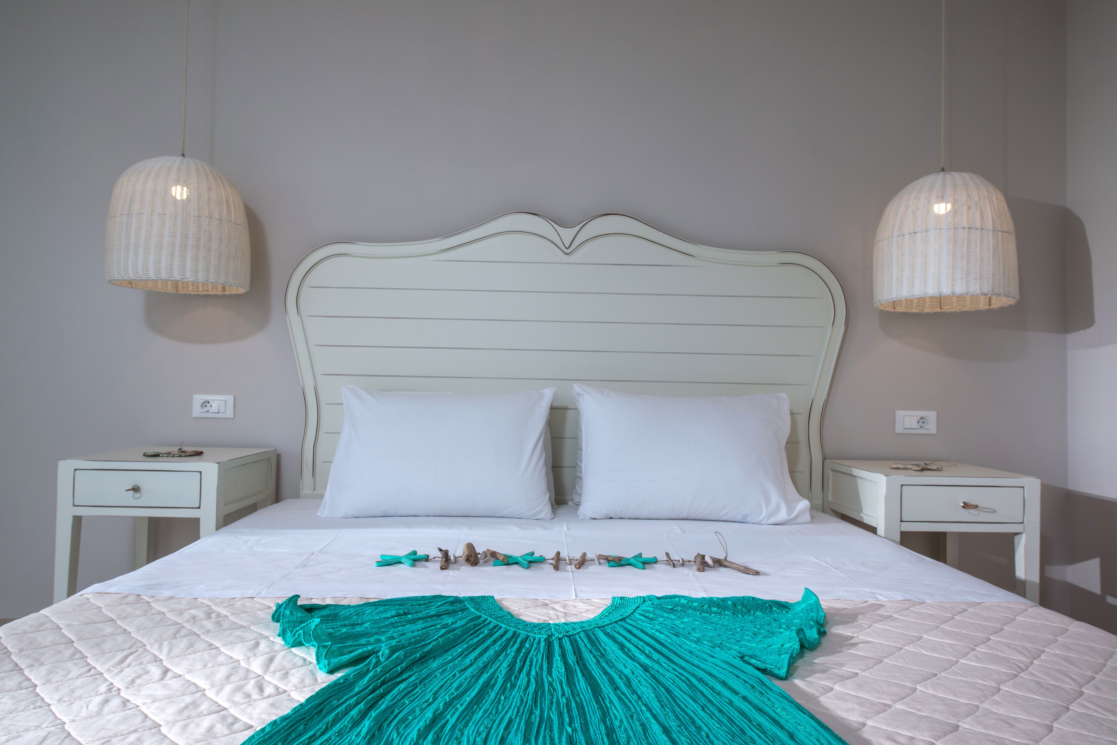A neatly made bed with a white headboard, two bedside tables, and two hanging lamps.