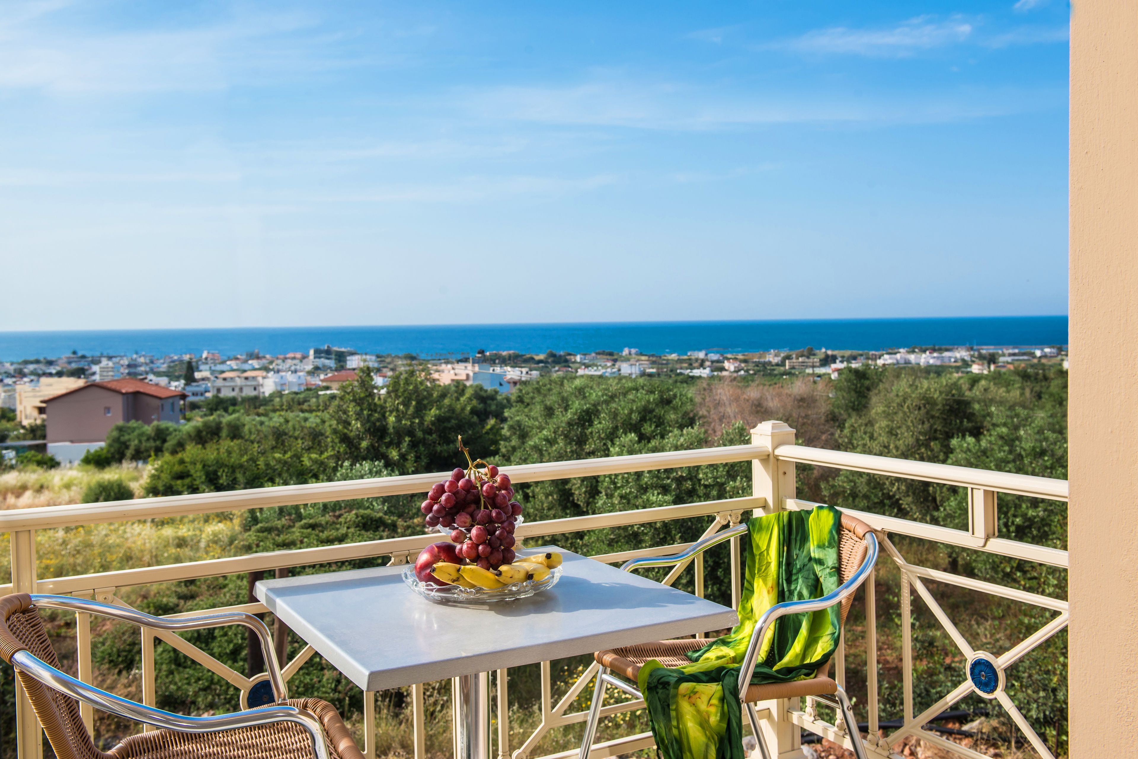 Un balcon avec une table, des chaises et une vue sur la mer et la ville.
