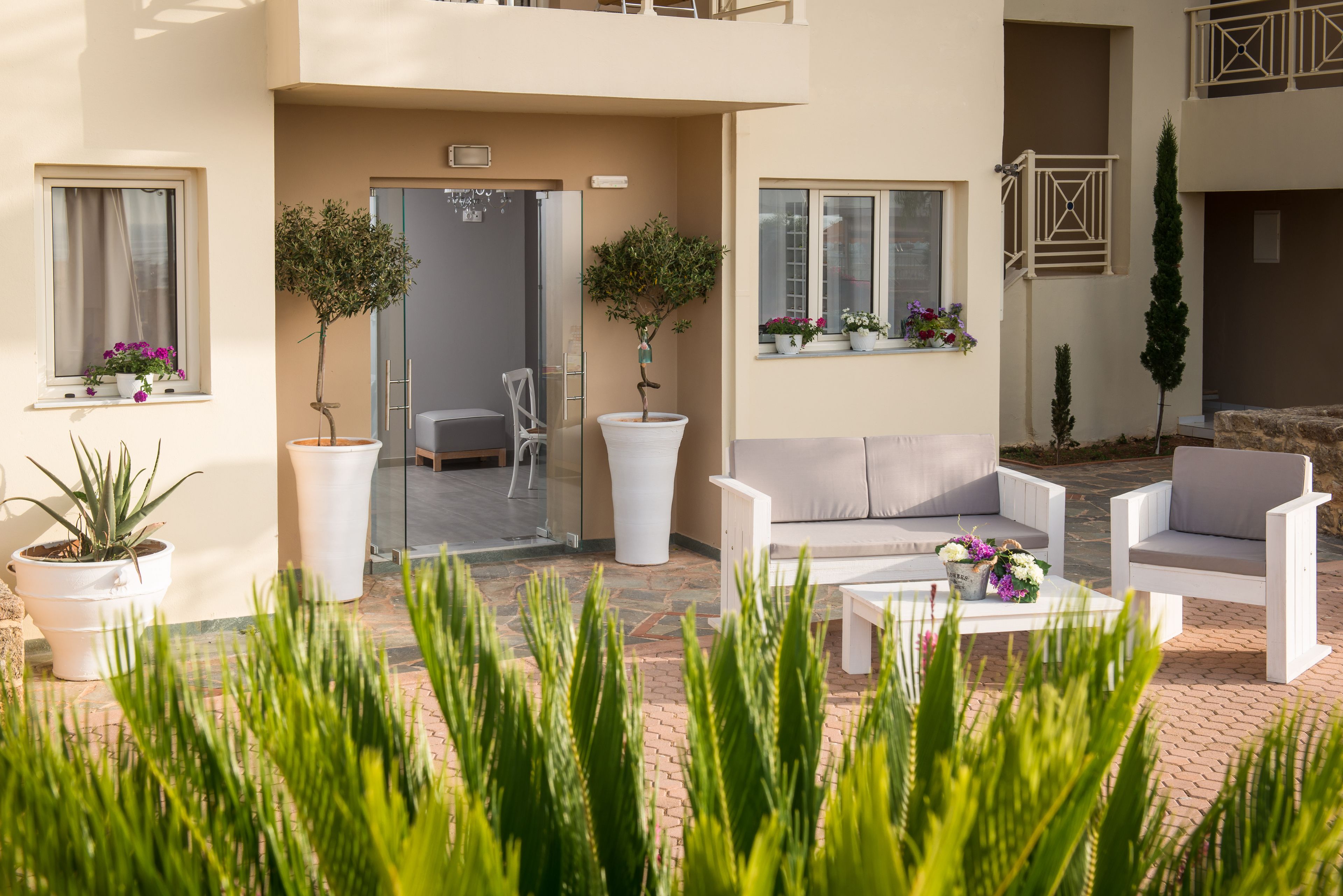 A modern outdoor seating area with white furniture, potted plants, and a clear view of the building's entrance.