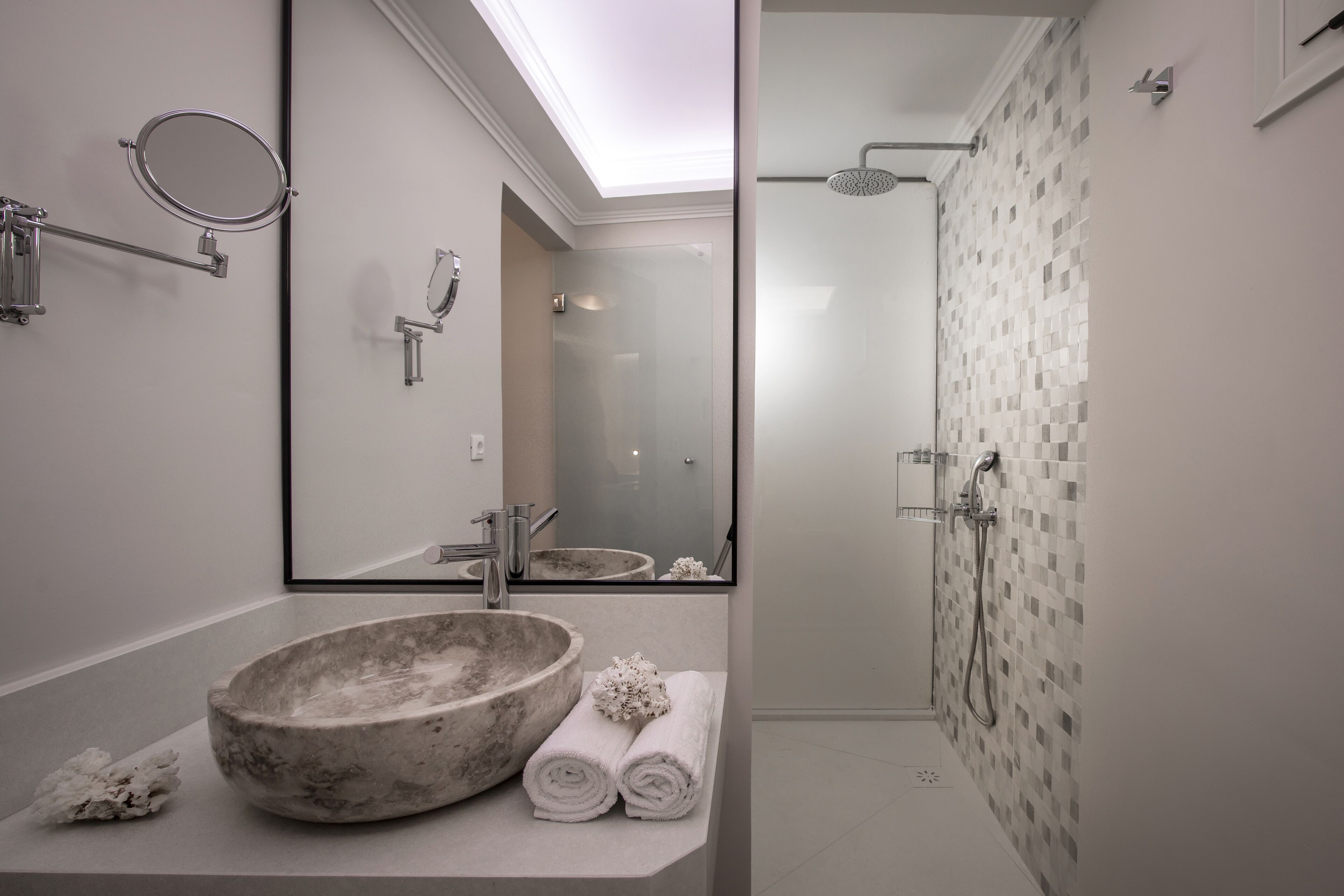 A bathroom with a large marble sink, a mirror, a towel rack, and a shower with a tiled wall.