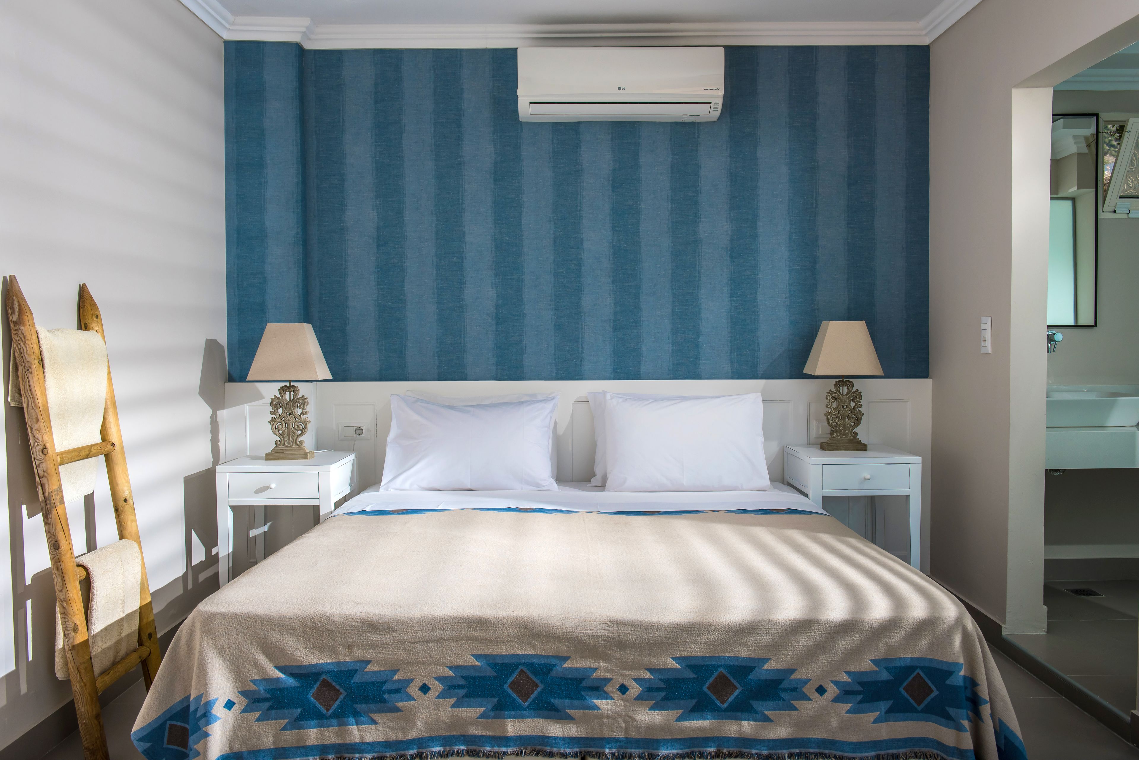Una habitación de hotel con cama, dos mesitas de noche, lámpara, escalera y aire acondicionado instalado en la pared.