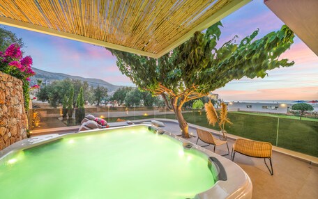 A hot tub area with a view of the sea and mountains, surrounded by outdoor seating and a pergola.