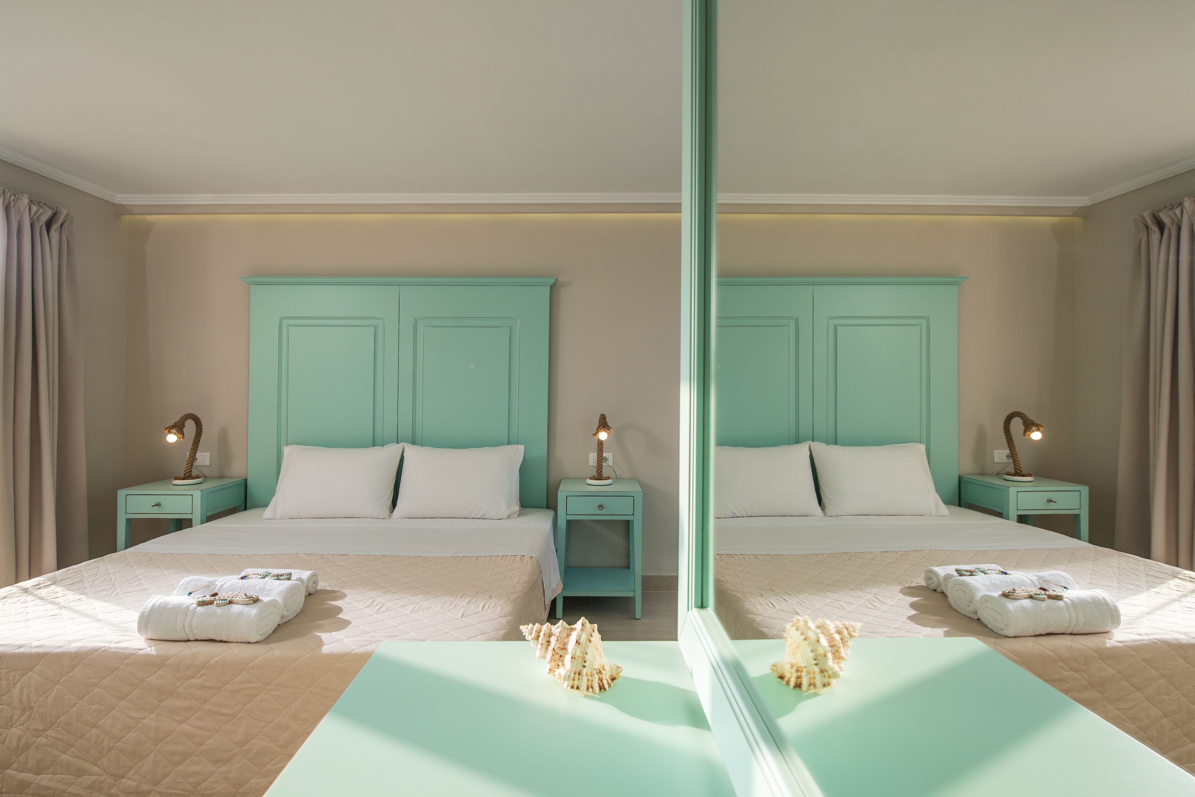 Ein Hotelzimmer mit Spiegel, zwei Betten, weißen Leinen, türkis-blauen Nachttischen und Lampen.