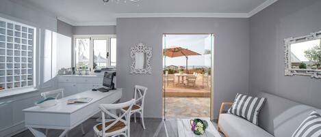 A modern kitchen with white cabinetry, a dining area with white chairs, and a grey sofa with striped pillows.