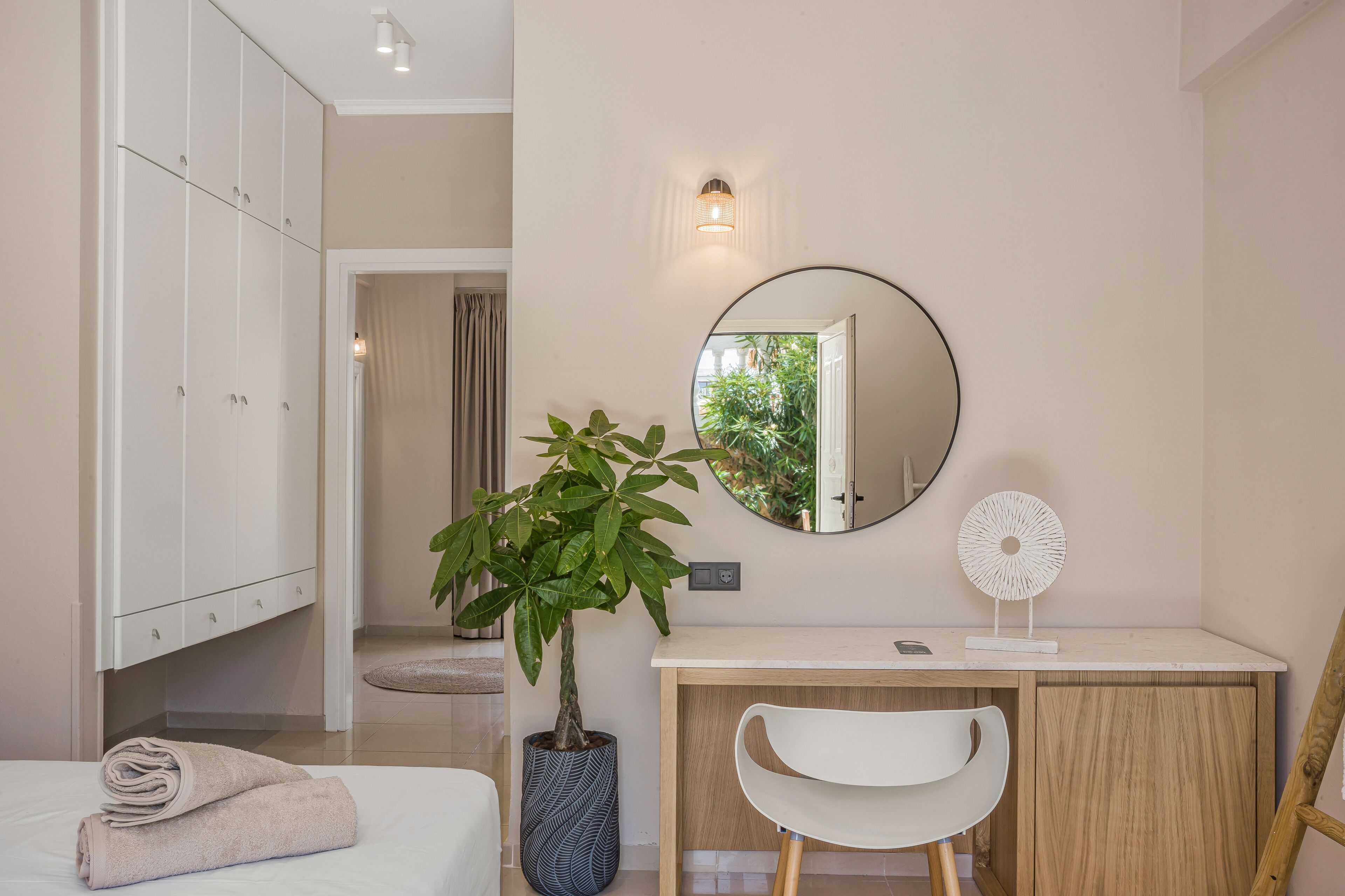 A modern bedroom with a bed, a desk, a chair, a potted plant, a mirror, and a wardrobe.