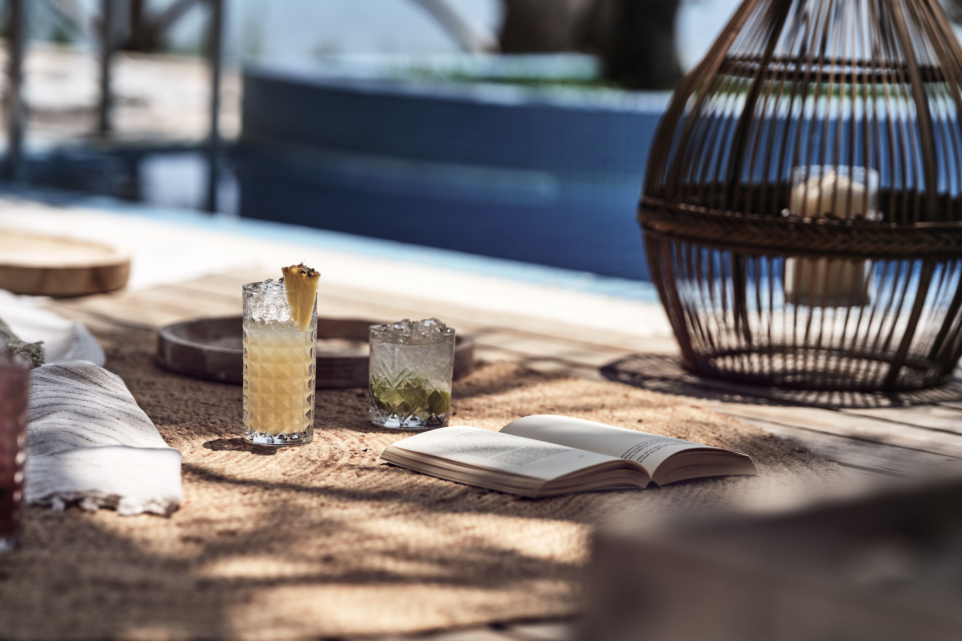 A sunlit outdoor setting with a wooden table, a wicker chair, and a book.