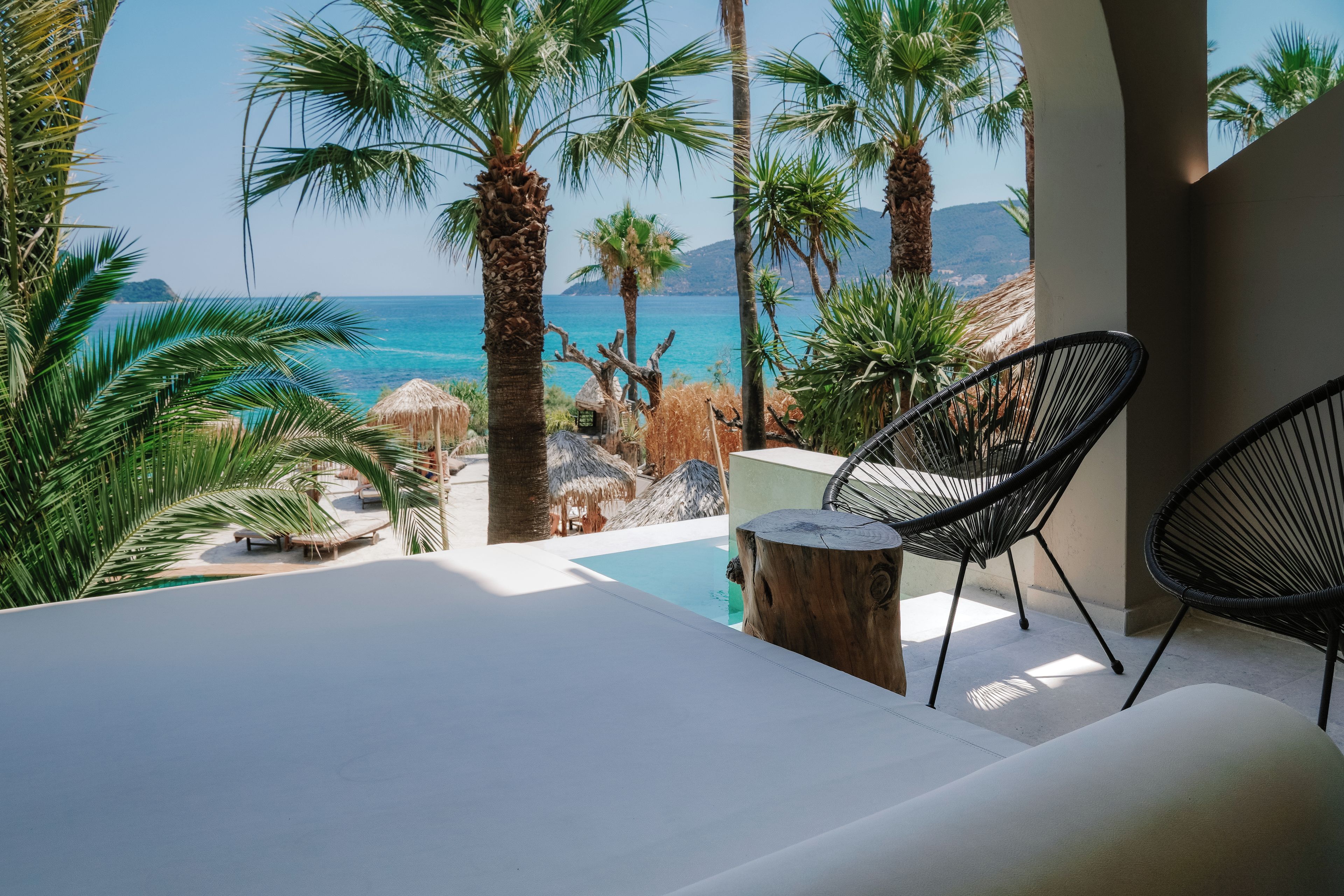 Un espace aménagé au bord de la piscine, avec des chaises longues, une vue sur la mer et une végétation tropicale.