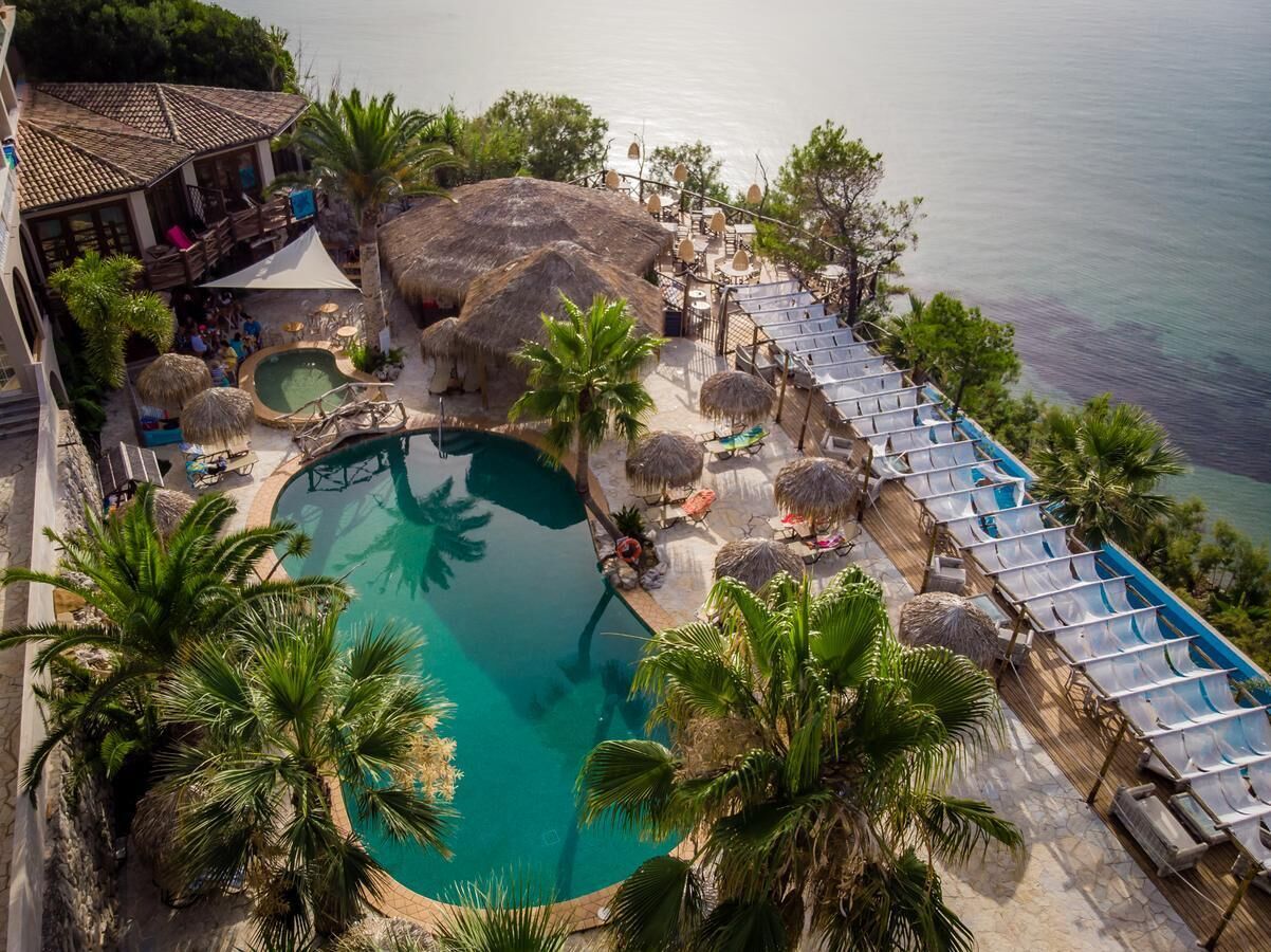 An aerial view of a resort with a large pool surrounded by palm trees and lounge chairs.