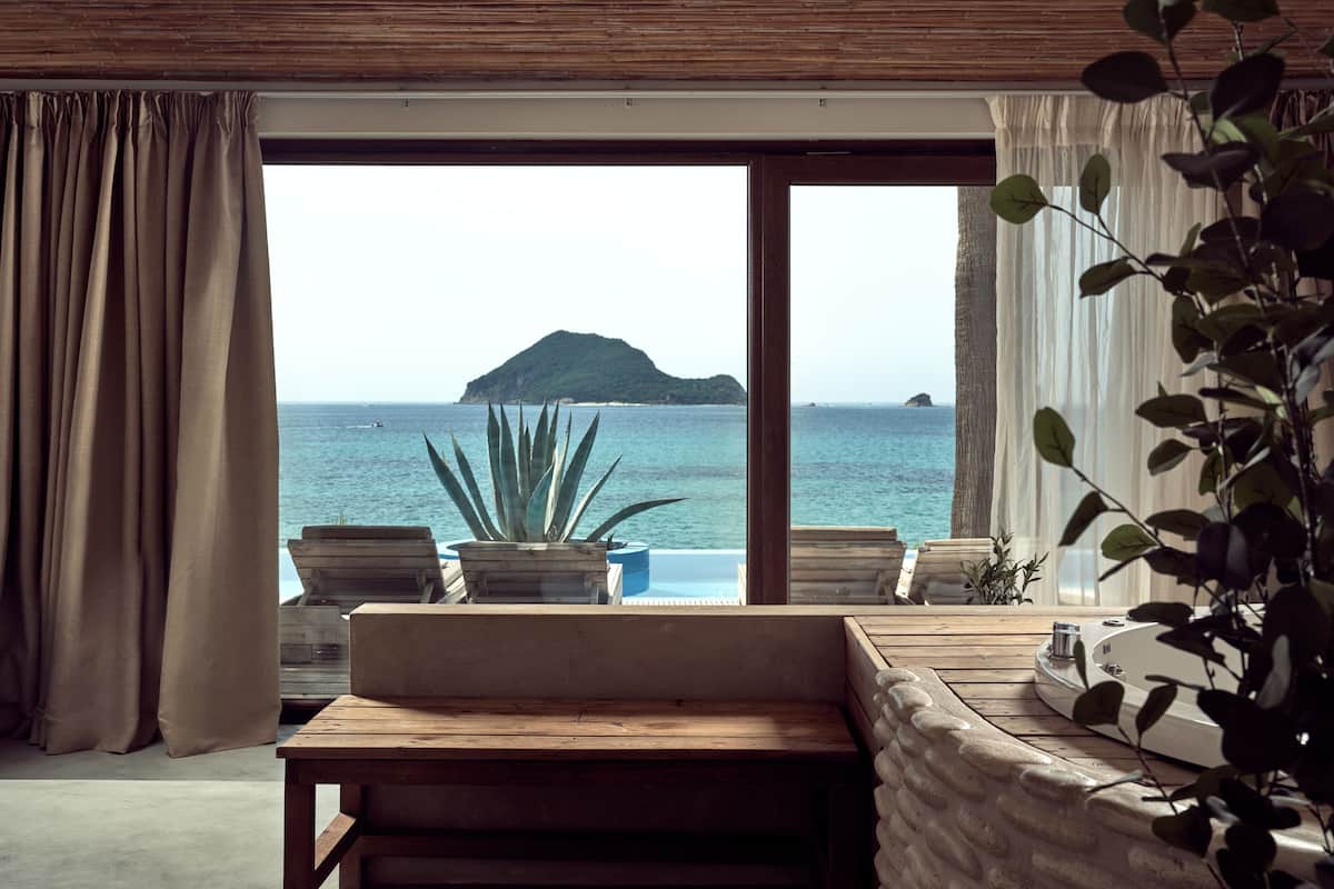 Ein Zimmer mit großem Fenster und Meerblick, mit einer Holzbank, einem Topfpflanzen und einer Badewanne.
