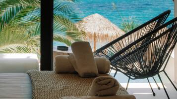 Una habitación con vista al mar, una cama, una silla y un paraguas de paja.
