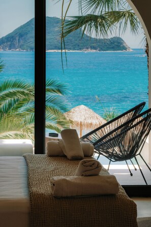 Une chambre avec vue sur la mer, un lit, une chaise et un parasol en chaume.