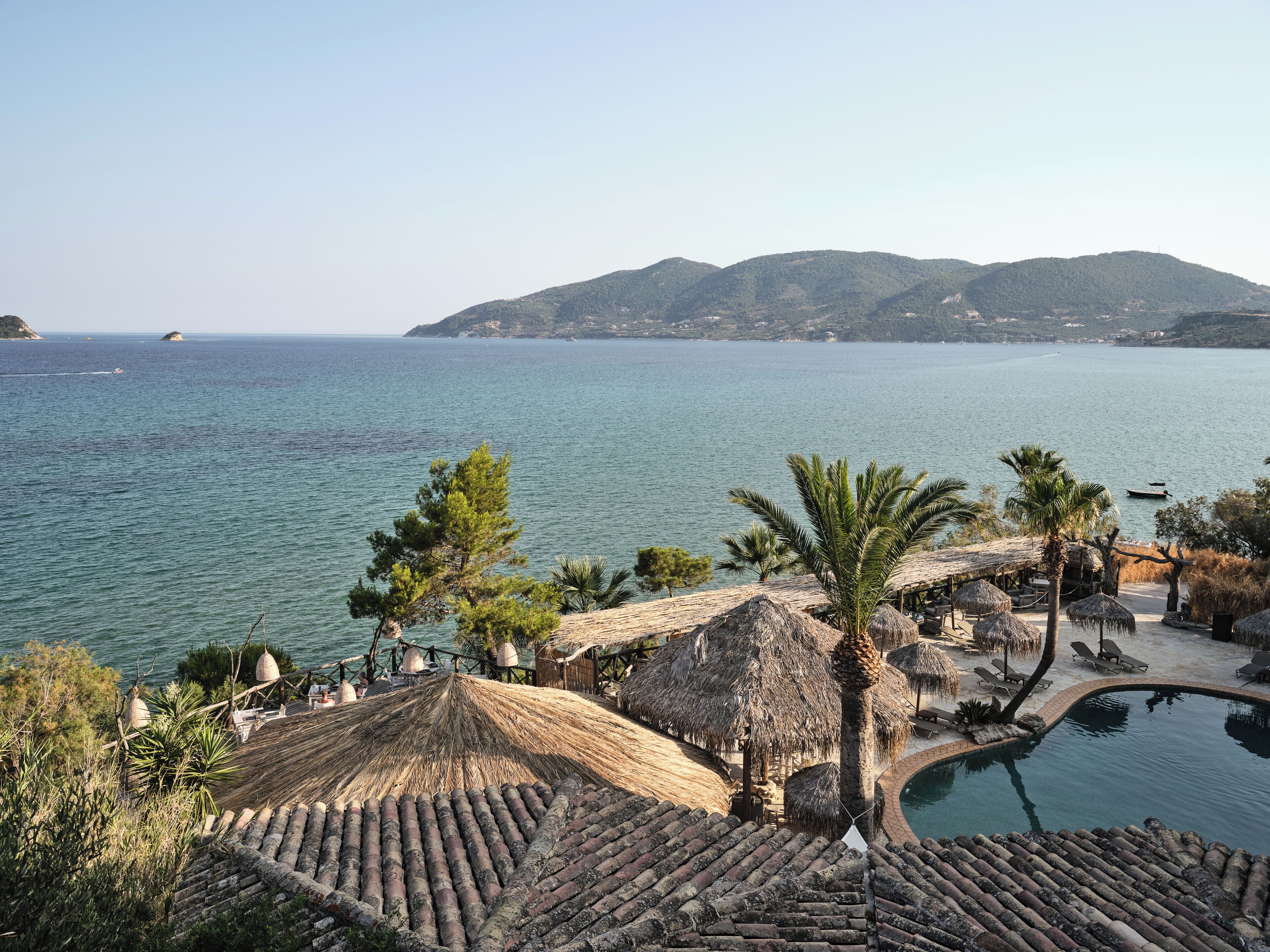 Ein Resort mit Pool, strohgedeckten Gebäuden und Blick auf das Meer.