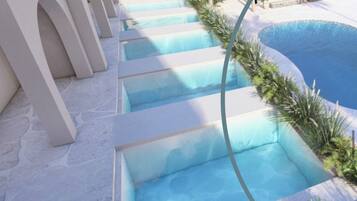 Zona de piscina con varios niveles de escalones que bajan al agua, rodeada de paredes blancas y vegetación.