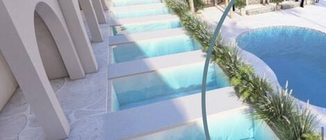 A pool area with multiple levels of steps leading into the water, surrounded by white walls and greenery.