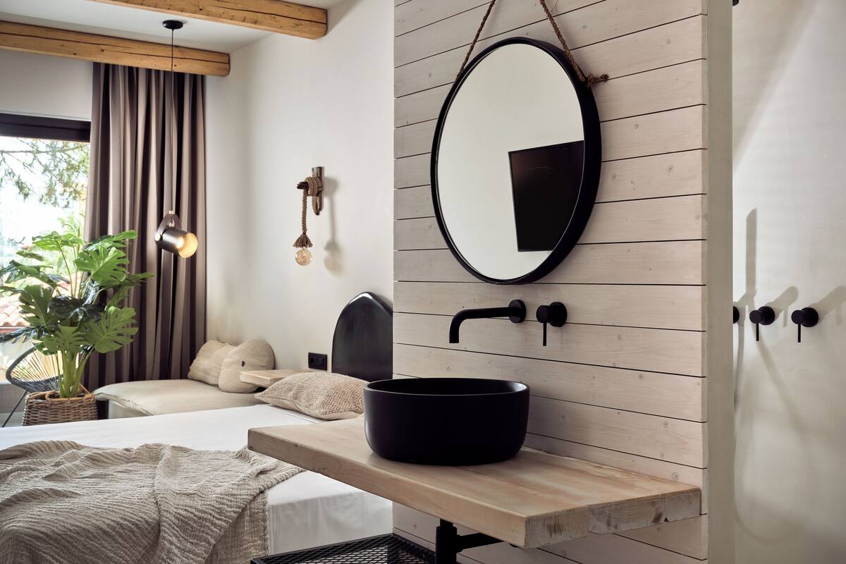 Ein modernes Badezimmer mit einer Holzvertäfelung, einem runden Spiegel, einem schwarzen Waschbecken und einem Nachttisch.